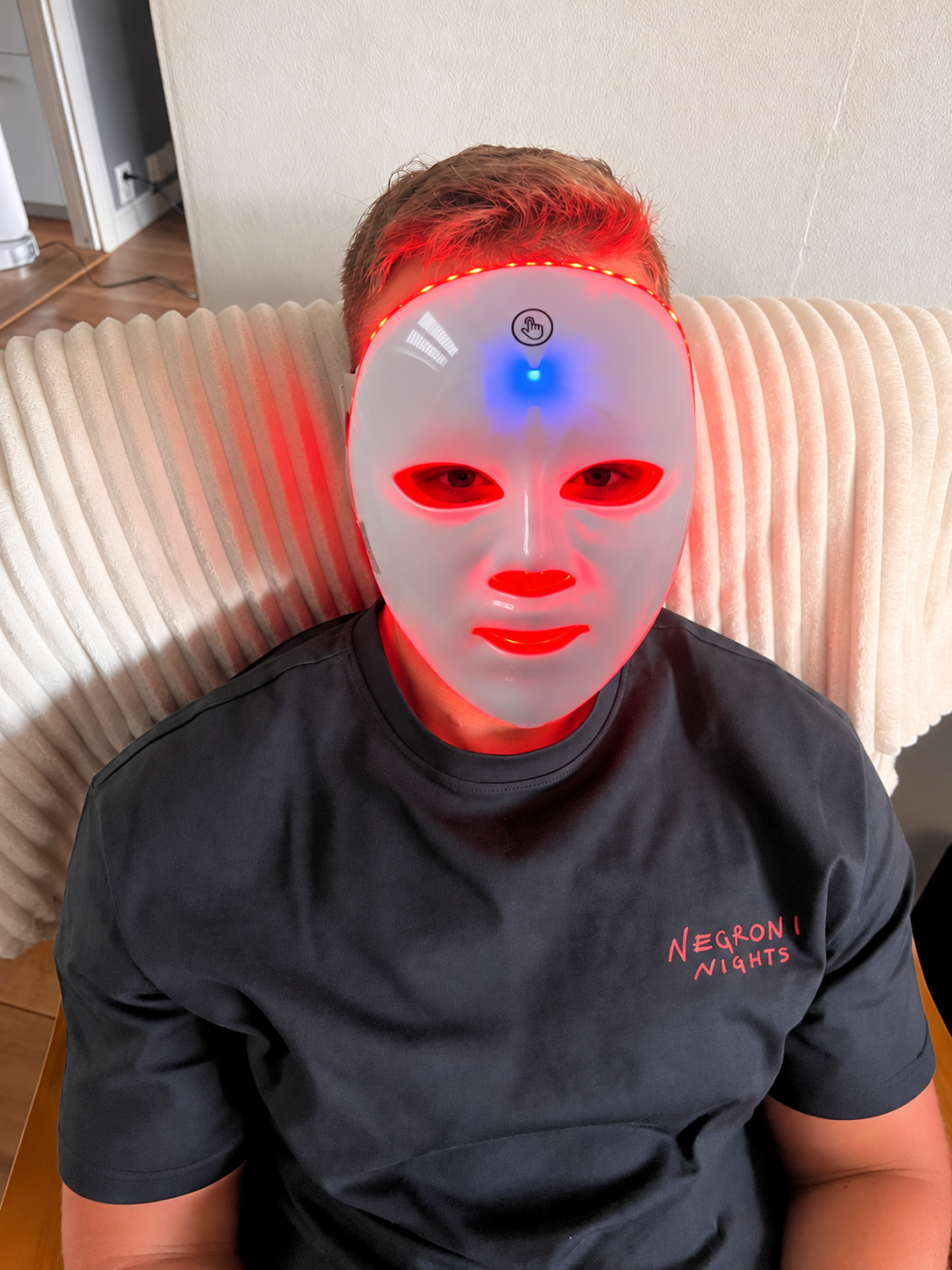 Man på en soffa med LED-masken i rött ljus
